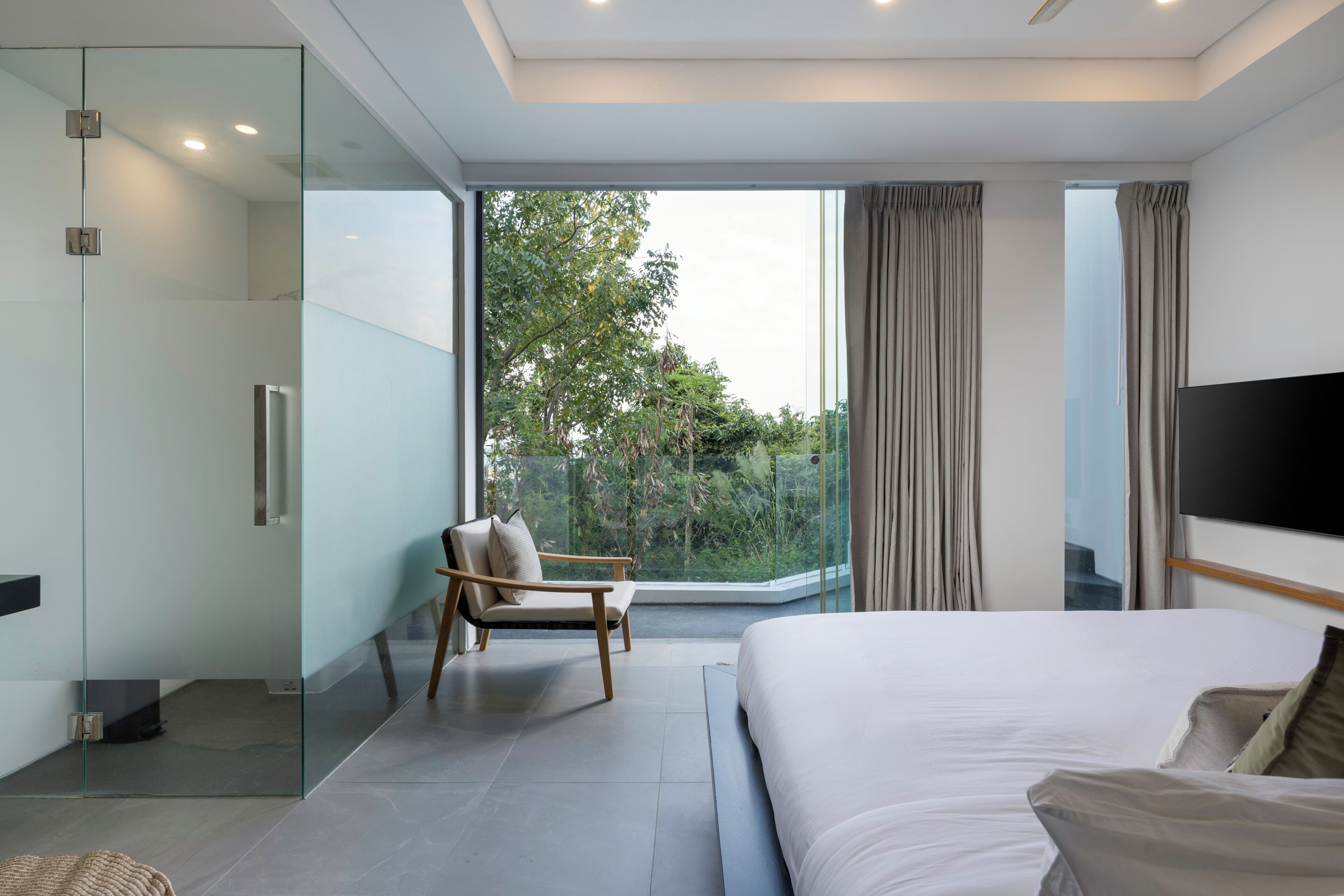 A modern hotel room with a large bed, a seating area, a glass shower enclosure, and a TV.