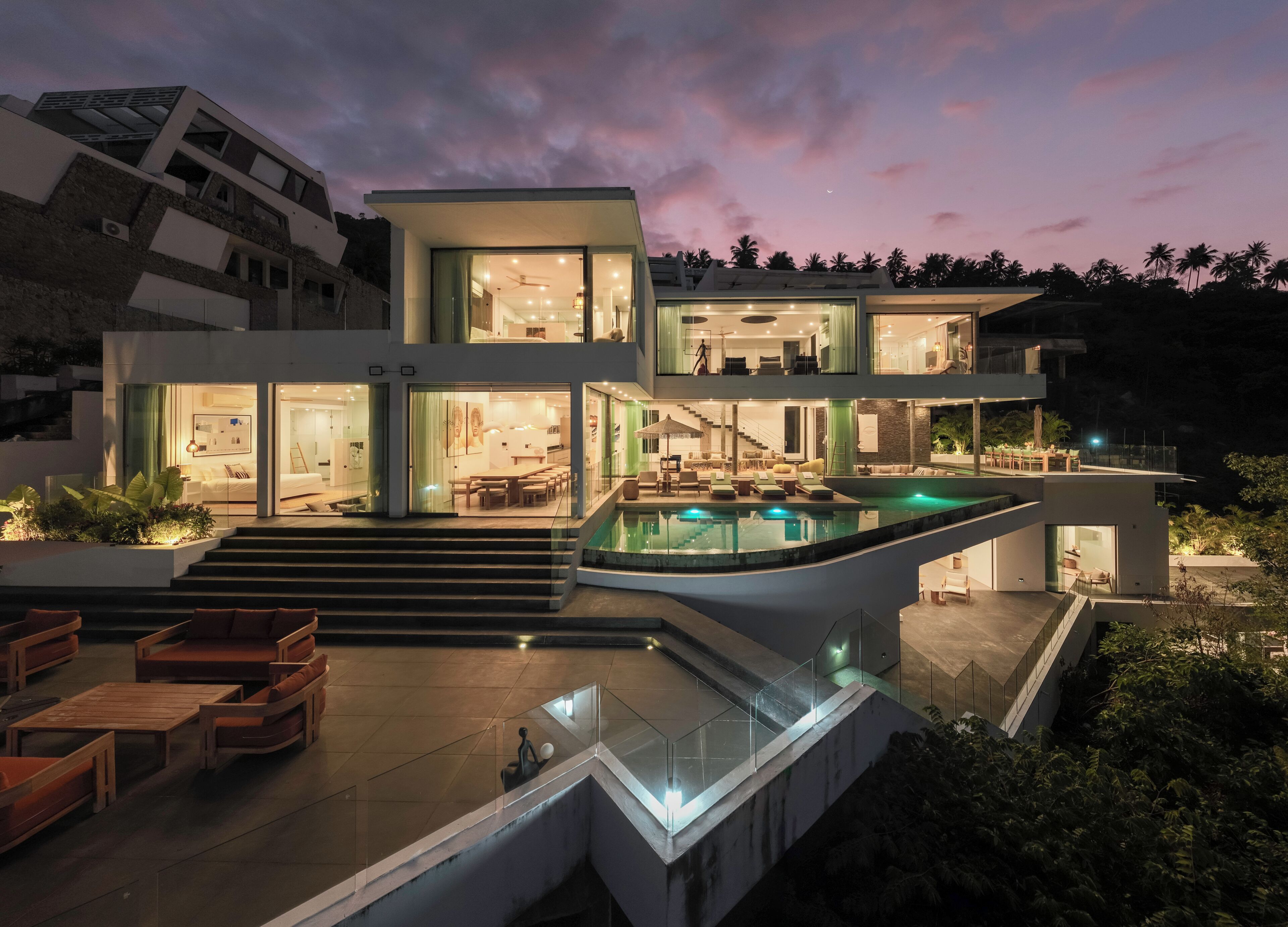A modern multi-story house with a swimming pool, outdoor seating, and a staircase leading to the upper levels.