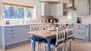 A kitchen with a dining table, chairs, cabinets, and a window with a view of trees. - Nether Clashnoir Glenlivet (Ballindalloch)