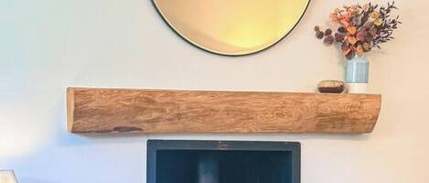 Un salon avec une cheminée, un miroir rond, une étagère en bois et une petite plante posée sur une table.