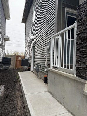 A residential building with a stone facade, a white railing, and a concrete pathway. - Selah’s Suite - Cozy Modern Getaway (Edmonton)