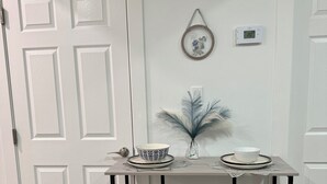 A small dining area with a table, two stools, a decorative plant, and a wall-mounted thermostat. - Selah’s Suite - (AC+Wifi+3beds(1 King bed +2 twin sofa beds ) (Edmonton)
