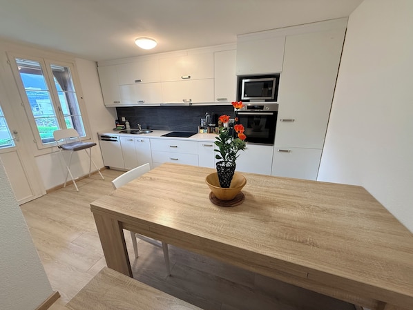 A modern kitchen with white cabinets, a wooden dining table, and a potted plant.
