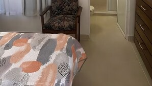 Um quarto com cama, cadeira, quadro, chuveiro e guarda-roupa.