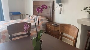 Quarto com cama, mesa de cabeceira, escrivaninha, cadeira, planta em vaso e luminária na parede.