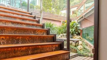 Una scala in legno conduce a una porta in vetro, con vista su un giardino e un edificio sullo sfondo.