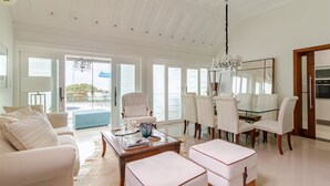 Amplia sala de estar con techo alto, comedor con sillas blancas y vistas a través de grandes puertas de vidrio.