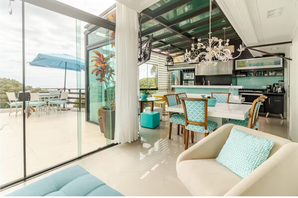 Un interior moderno con comedor, cocina y un amplio ventanal corredera que da a un patio exterior.