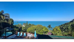 Una terraza con sillones y una mesa, con vista a un paisaje costero con árboles y vistas al mar.