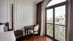 Quarto de hotel com cama, escrivaninha, cadeira, telefone e varanda com vista para edifícios.