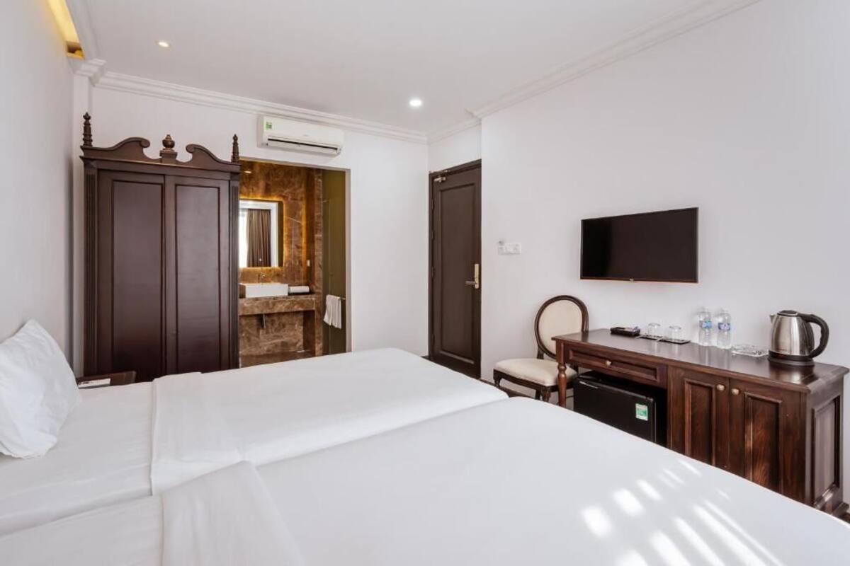 A hotel room with a bed, a wooden wardrobe, a desk with a television, and a small bathroom.