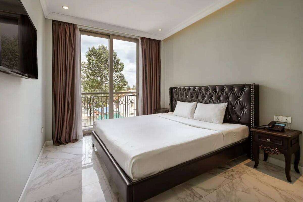 A hotel room with a large bed, a nightstand, a TV, and a balcony with a railing.
