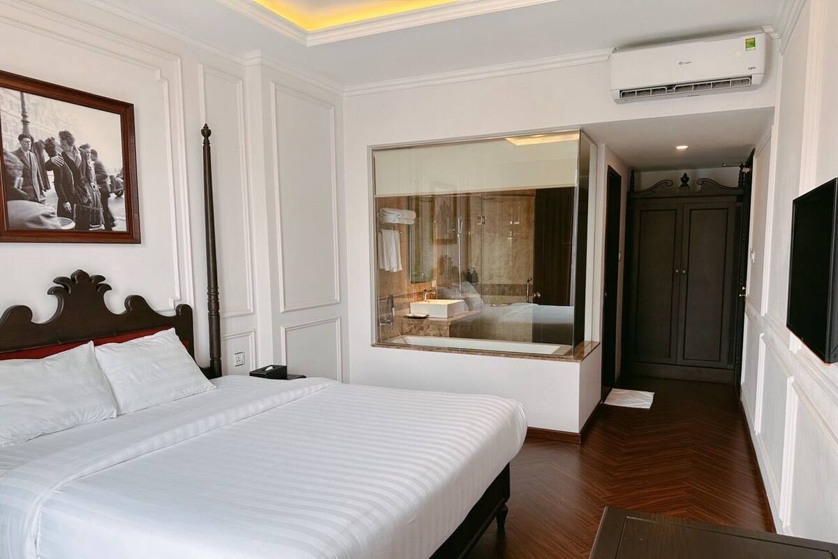 A hotel room with a large bed, a mirror, an air conditioning unit, and a television.