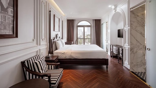 Quarto de hotel com uma cama grande, um sofá, uma TV e uma parede de mármore.