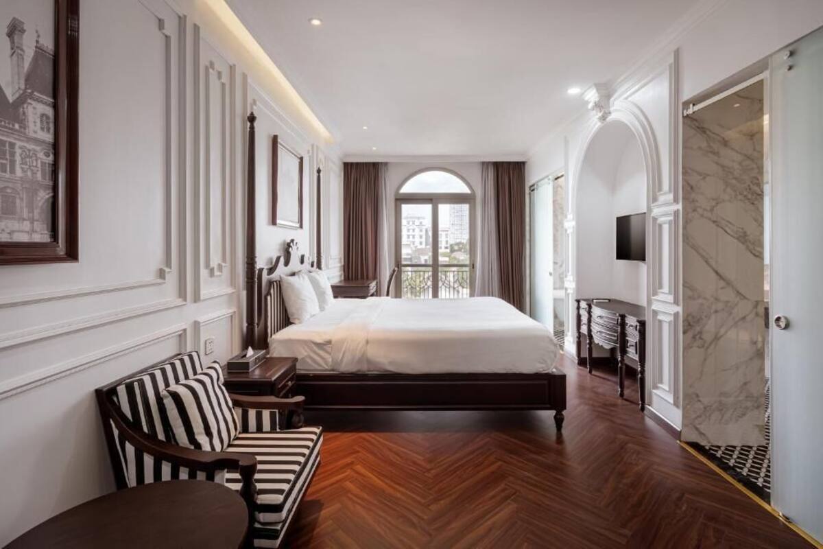 A hotel room with a large bed, a sofa, a TV, and a marble wall.