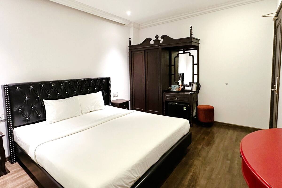 A hotel room with a large bed, a dresser, a mirror, and a red chair.