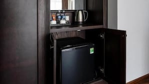 Quarto compacto com geladeira embutida, uma cafeteira pequena e um espelho sobre o balcão.