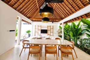 A spacious dining area with a large wooden table, wicker chairs, a ceiling fan, and a TV mounted on the wall. - Villa Toro - Bingin Bali (Pecatu)