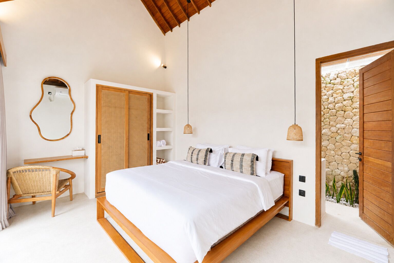 A bedroom with a wooden bed, a wicker chair, a wardrobe, and a stone wall.