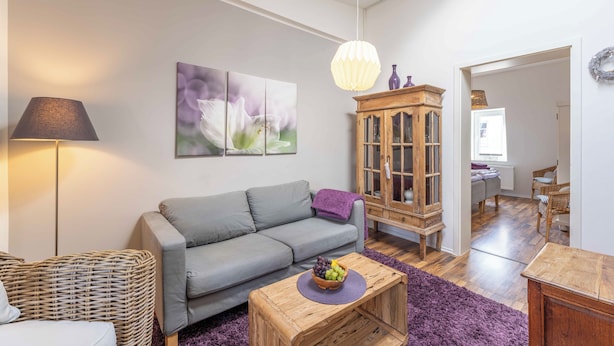 En stue med en grå sofa, et træskab, en lampe og en lilla måtte.
