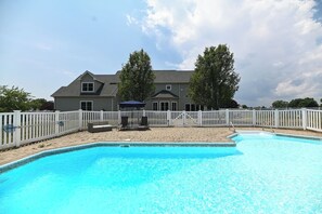 A swimming pool with a white fence, a house in the background, and a cloudy sky.