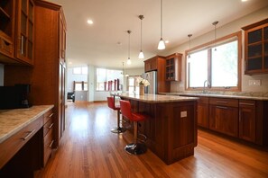 A spacious kitchen with wooden cabinets, a large island with bar stools, and pendant lighting.