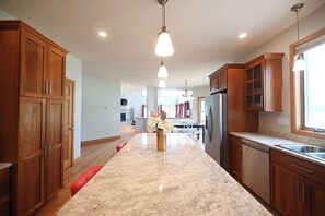 A kitchen with wooden cabinets, a marble countertop, a refrigerator, and pendant lighting.