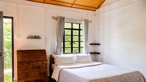 Un dormitorio con un aparador de madera, una cama con colcha de lunares, una ventana con cortinas y vistas al exterior.