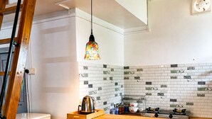 Una cocina con una isla de madera, azulejos blancos tipo metro, una lámpara colgante de colores, una estufa a gas y dos taburetes.