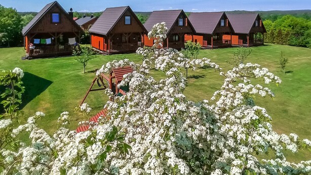 A row of wooden cabins with red accents, a grassy lawn, and a wooden swing set. - Lovely home in Ko1czewo (Ko1czewo)