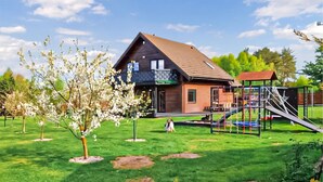 A house with a sloped roof, a porch, and a playground with a slide and climbing structure. - Lovely home in Ko1czewo (Ko1czewo)