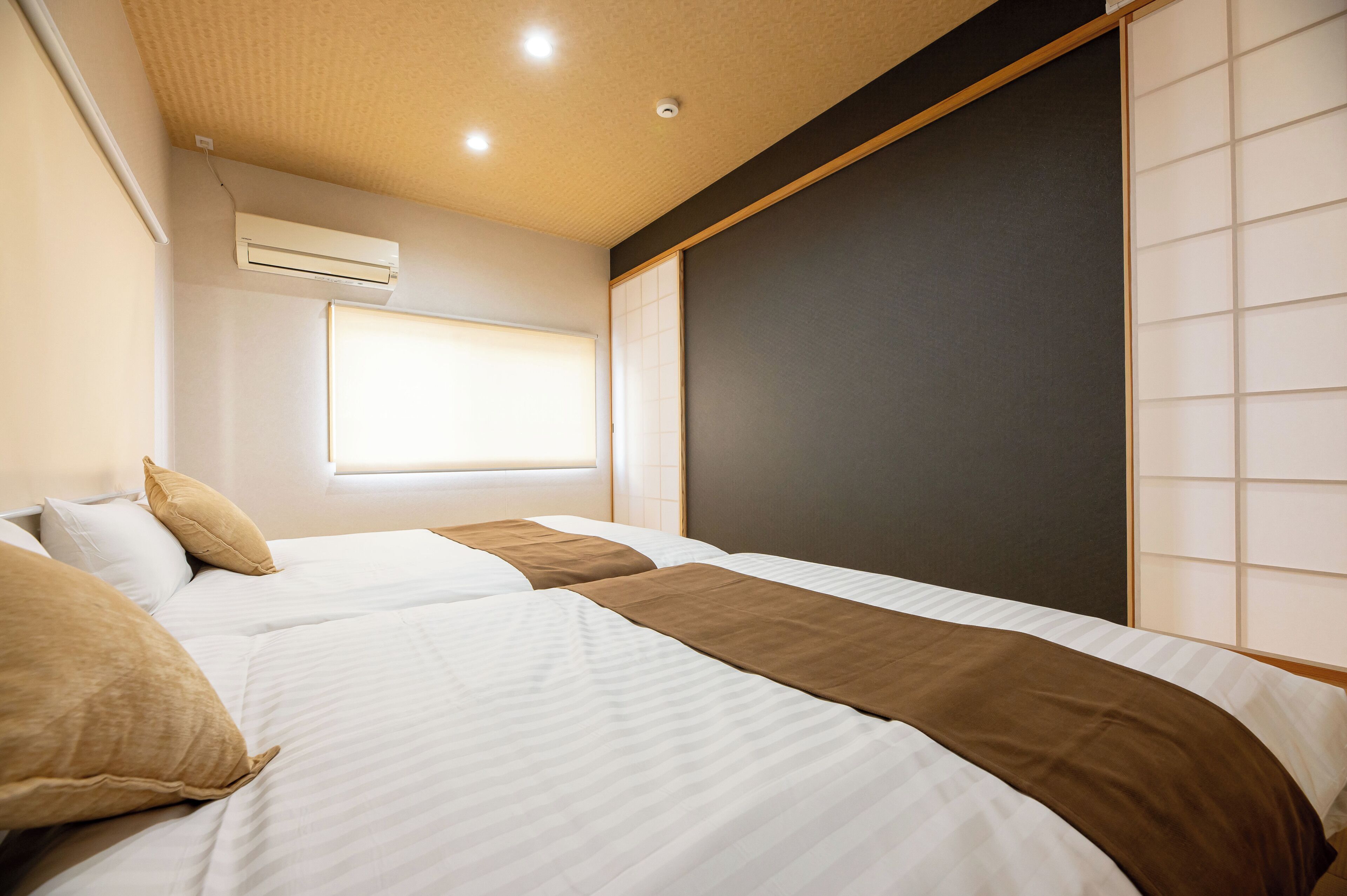 A hotel room with two beds, a window with blinds, an air conditioning unit, and a sliding door.