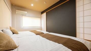 A hotel room with two beds, a window with blinds, an air conditioning unit, and a sliding door.