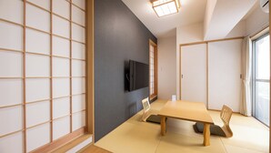 A traditional Japanese room with tatami flooring, a low table, and a television mounted on the wall.
