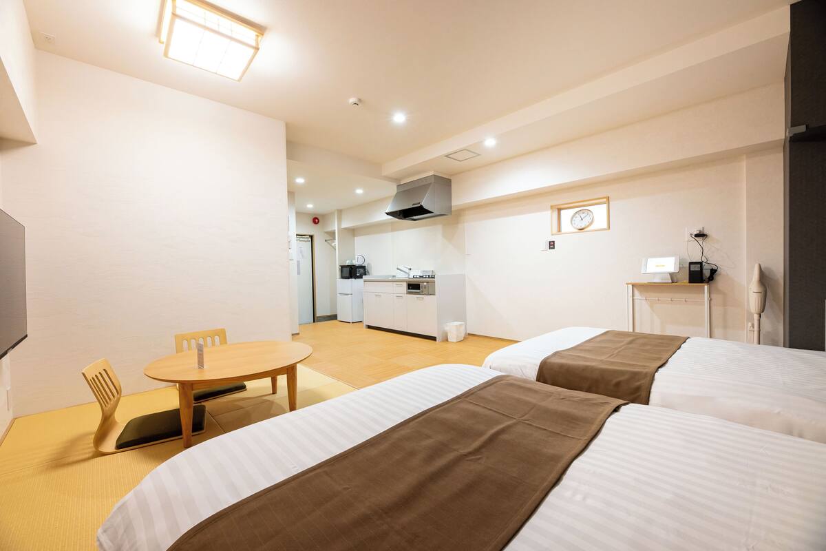 Habitación de hotel con dos camas, una pequeña mesa de comedor, kitchenette y televisión.