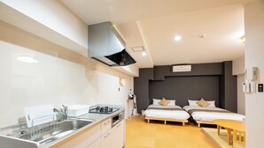 A compact hotel room with a kitchenette, two single beds, a small dining table, and a built-in heater.