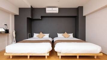 Ett modernt hotellrum med två separata sängar, en inbyggd luftkonditioneringsanläggning, ett nattduksbord och ett litet skrivbord med en lampa.