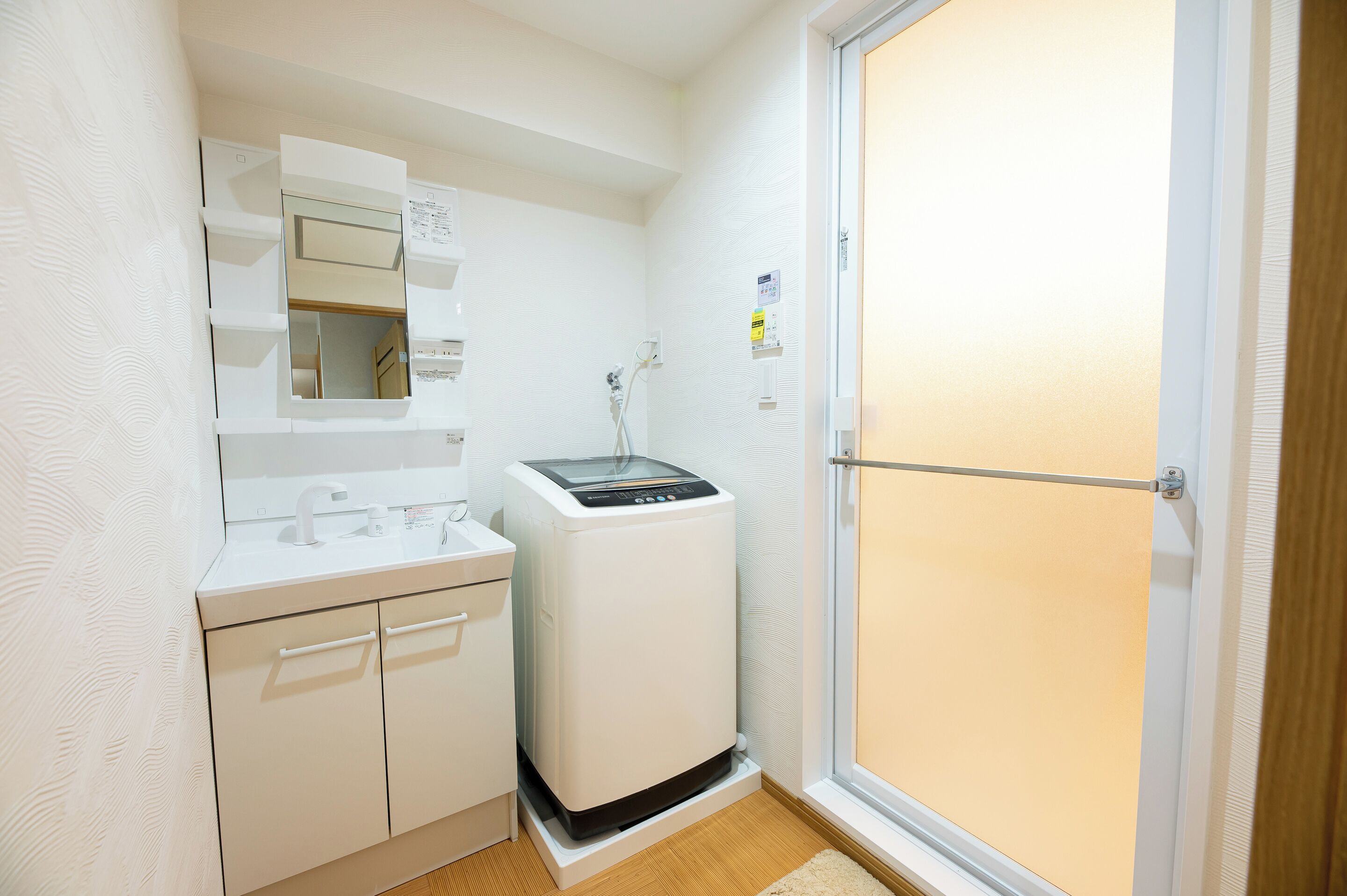 Een kleine badkamer met een ingebouwde wasmachine, een spiegel en een douche.