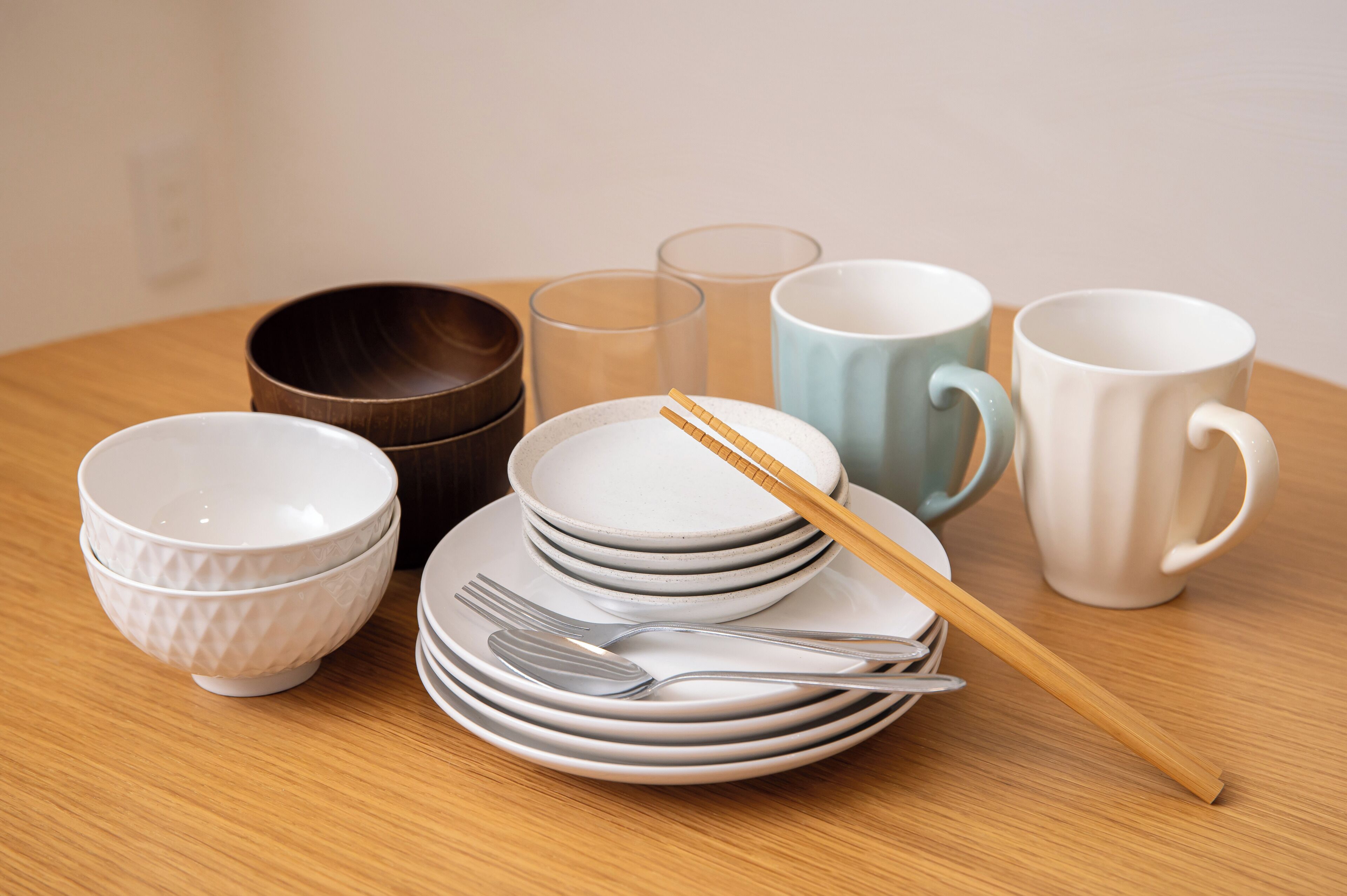 A table with stacked plates, bowls, glasses, and chopsticks.