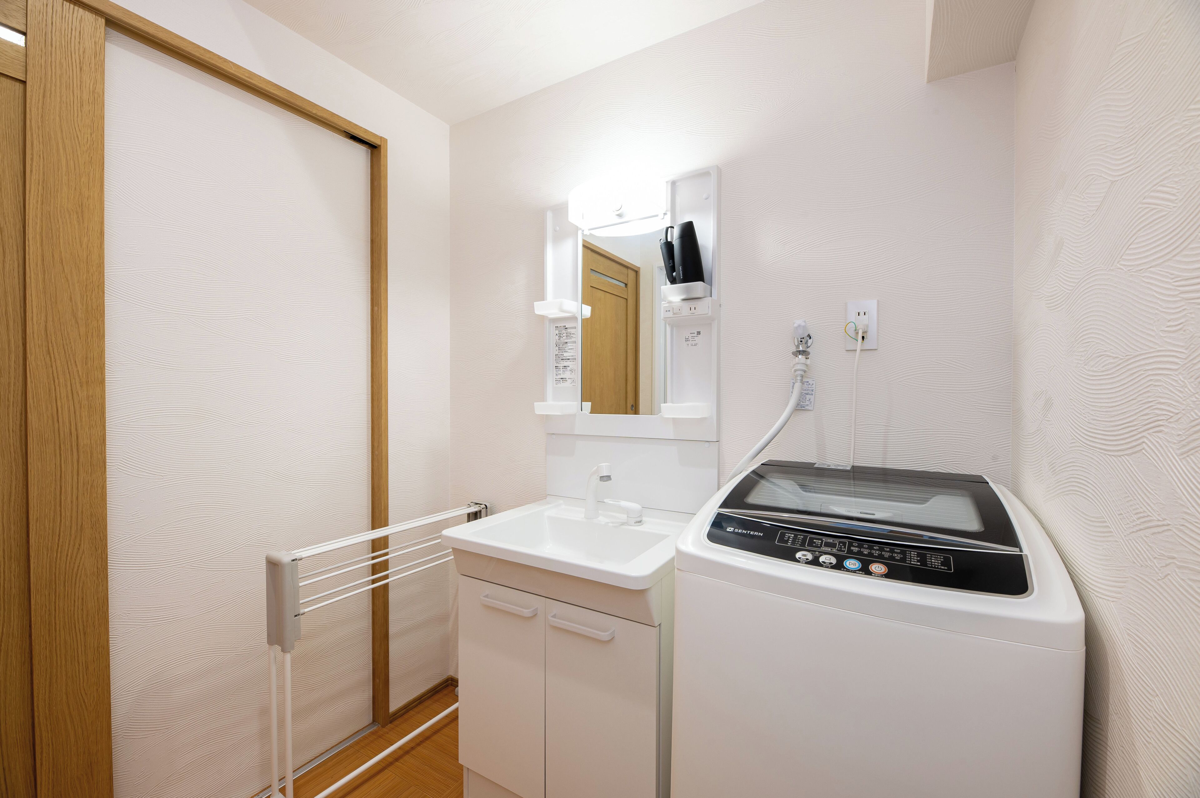 A compact bathroom with a sink, mirror, towel rack, and a washing machine.