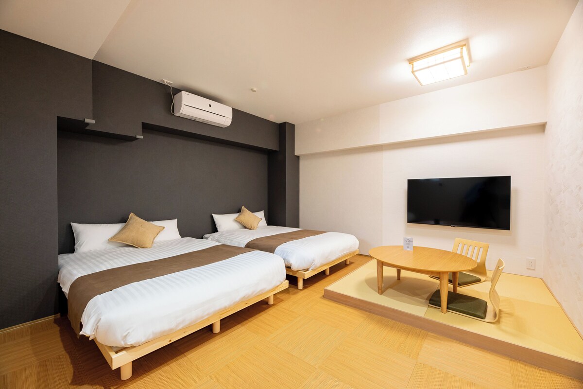 A hotel room with two beds, a TV, a table, and a chair.