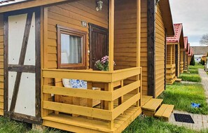 Een rij houten bungalows met een balkon, een raam met gordijn en een bord met het nummer '14'.