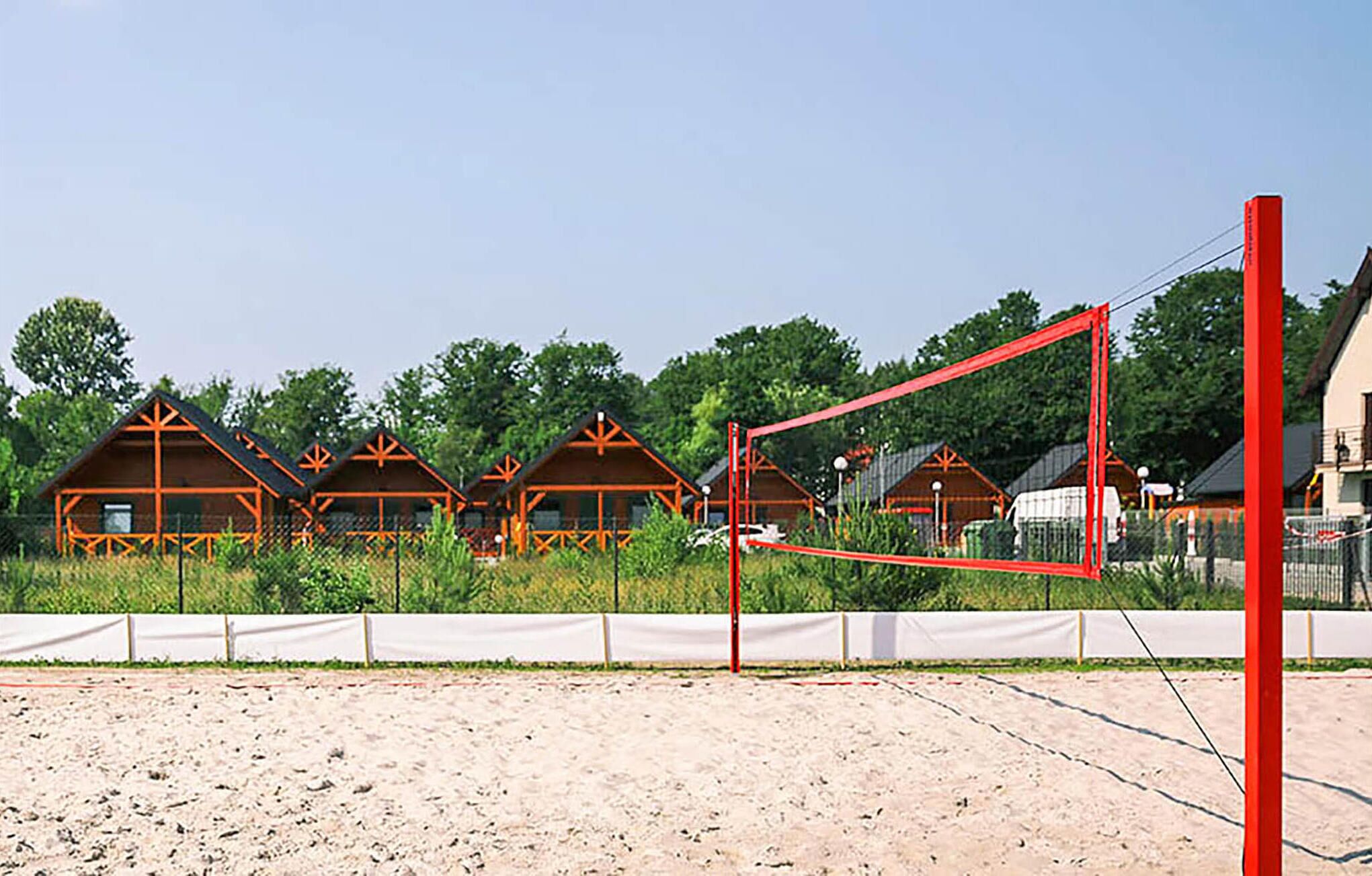 Een sportveld met een volleybalnet, omringd door houten vakantiehuisjes met een eenvoudig ontwerp.