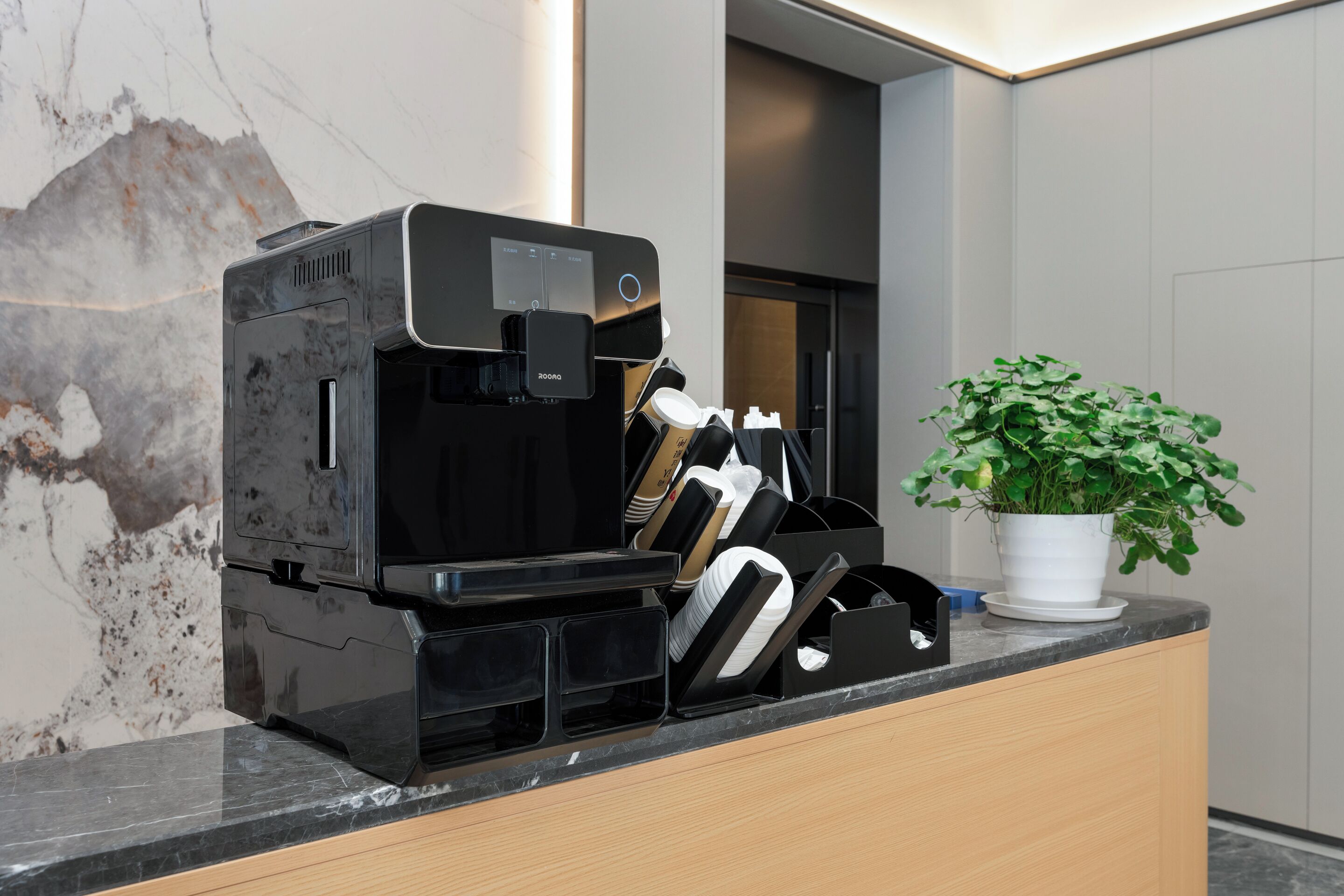 Eine moderne Kaffeemaschine, ein Topfpflanze und eine Theke mit einer marmorähnlichen Oberfläche.