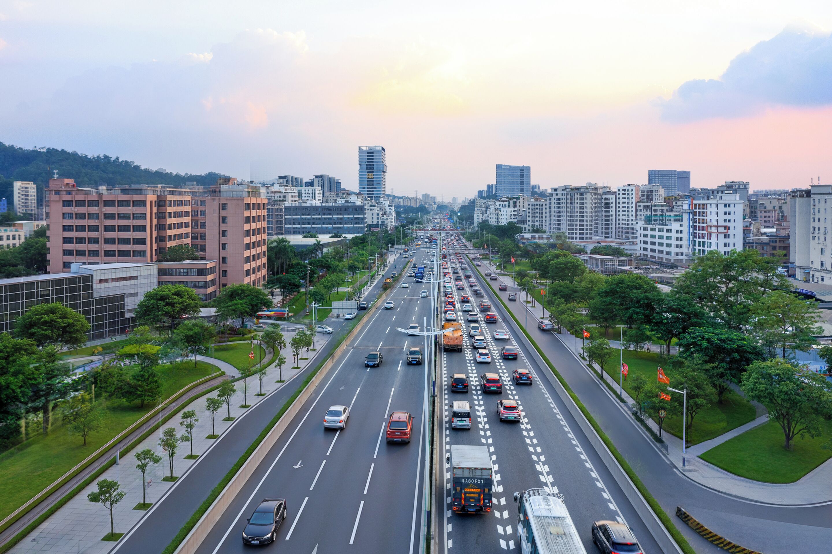 A multi-lane highway with vehicles, surrounded by modern buildings and greenery.