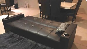 En svart lädersoffa med ett tillhörande fotstöd, ett litet runt bord och en mönstrad kudde.