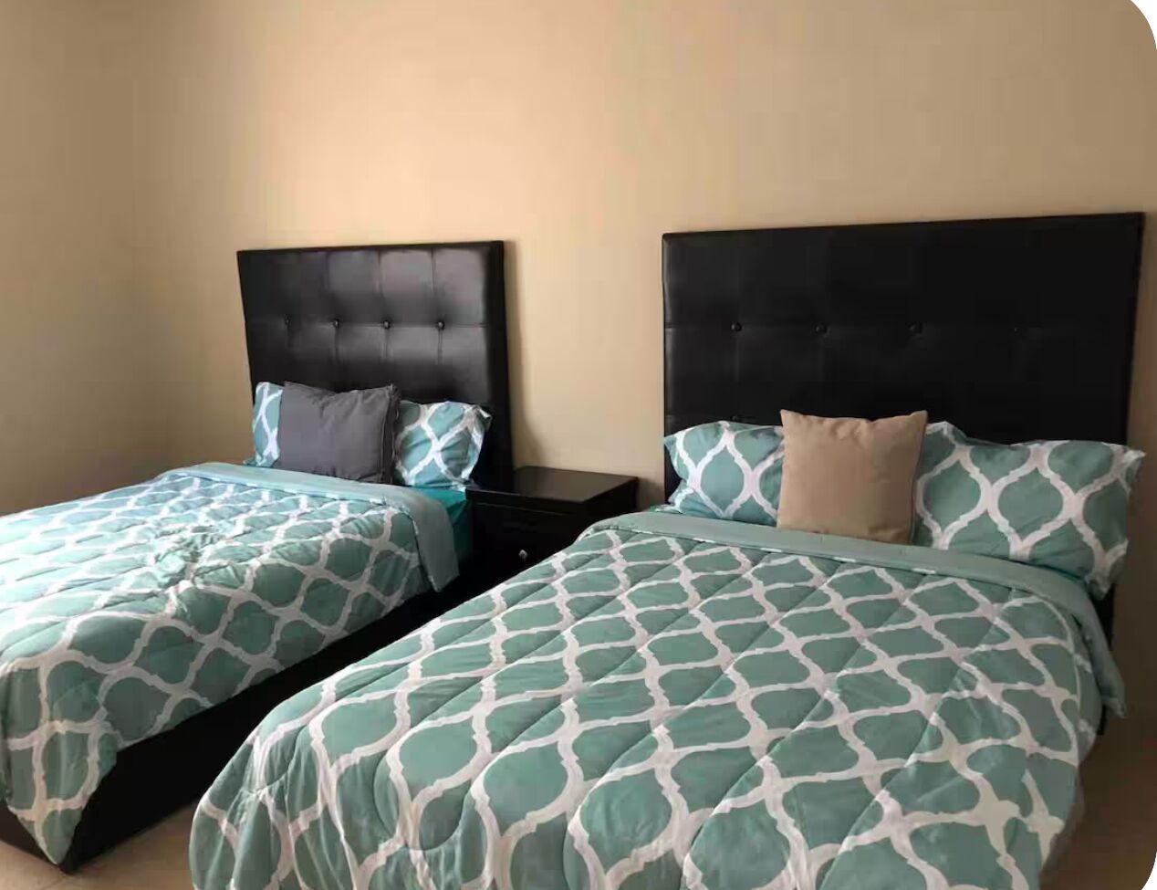 Duas camas de solteiro com cabeceiras iguais e roupa de cama estampada em um quarto de hotel.