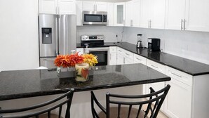A modern kitchen with white cabinets, stainless steel appliances, a granite countertop, and two black chairs.