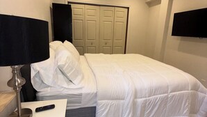 A bedroom with a bed, a bedside table with a lamp, a TV mounted on the wall, and a wardrobe.
