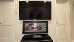 A room with a flat-screen TV mounted on the wall, a framed painting below it, and a black entertainment unit in the center.